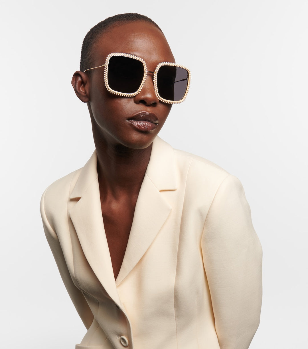 Rhinestone-trim sunglasses with dark lenses on a model wearing a cream blazer