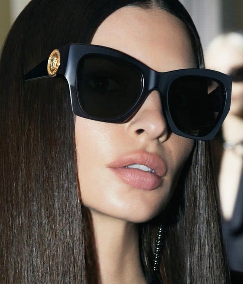 Black oversized sunglasses with dark lenses, gold logo temples, on model