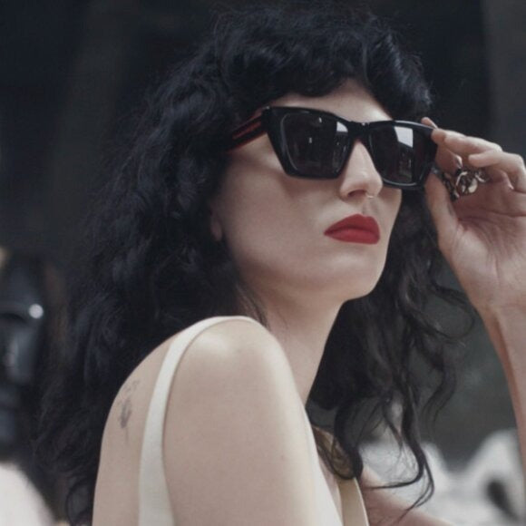 Black cat-eye sunglasses with dark lenses on model, red temple accents
