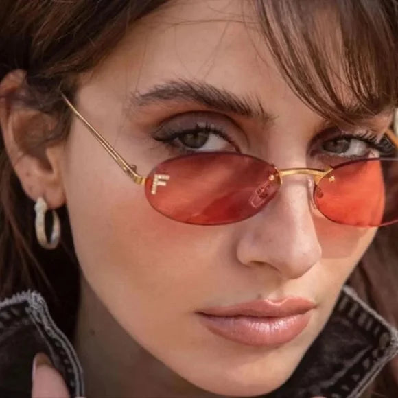 Close-up of gold thin-frame round sunglasses with red tinted lenses and F detail