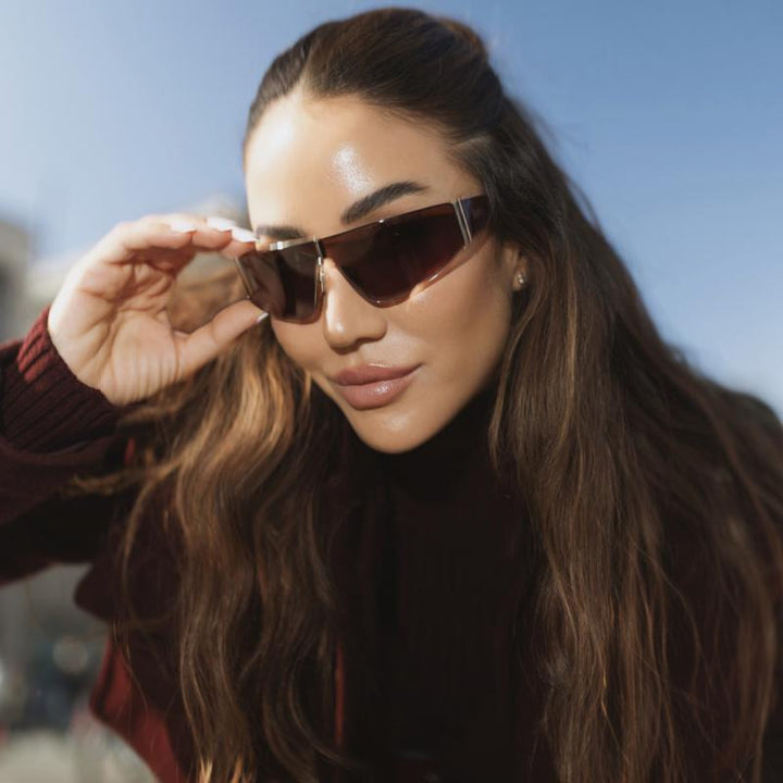 Brown shield sunglasses with gold-tone trim, shown close-up on a model.