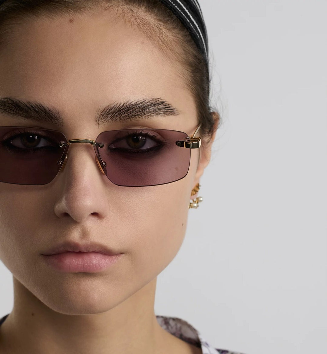 Dior rimless sunglasses on face, tinted pink lenses and gold-tone frame