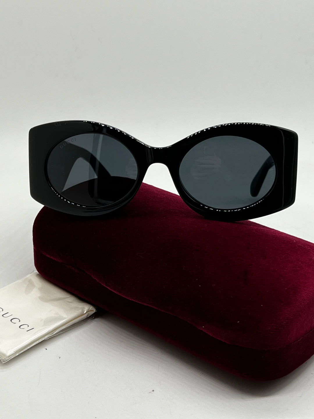 Black thick-rim rectangular sunglasses with dark lenses on burgundy case.