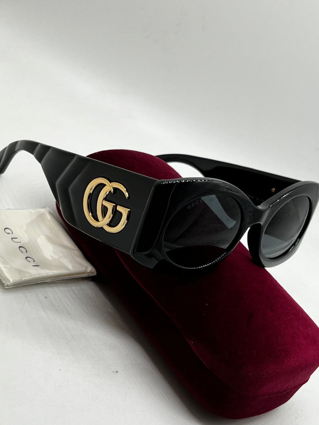 Black Gucci sunglasses with gold GG emblem and quilted temples on case with cloth.